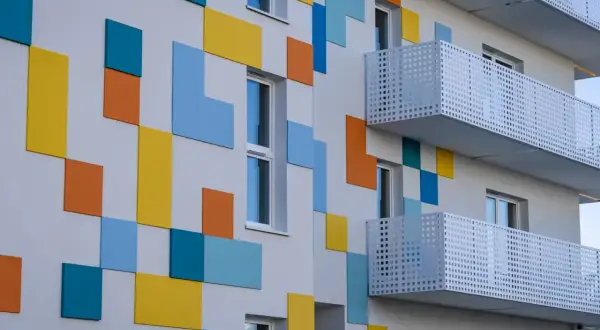 Nowoczesny budynek z kolorowymi, geometrycznymi panelami i białymi balkonami.