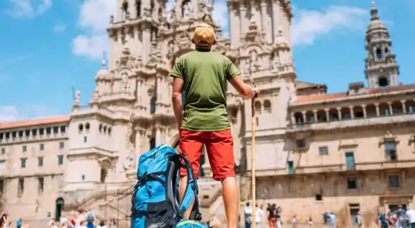 Pielgrzym z plecakiem i laską przed katedrą w Santiago de Compostela. Święta w El Camino to cel podróży.