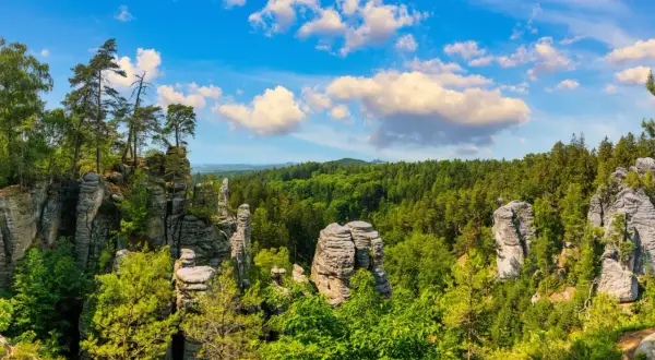 Felsformationen und grüne Wälder laden zum tschechien wandern ein. Ein malerischer Ausblick unter blauem Himmel mit Wolken.
