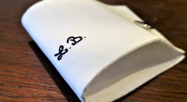 Un dettaglio di una camicia bianca piegata, con le iniziali "F.B." ricamate in nero.