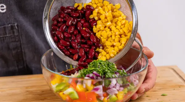 Kidneybohnen und Mais werden in eine Schüssel mit Paprika, Zwiebeln und Kräutern gegeben. Ein bunter Kidneybohnen Salat entsteht.