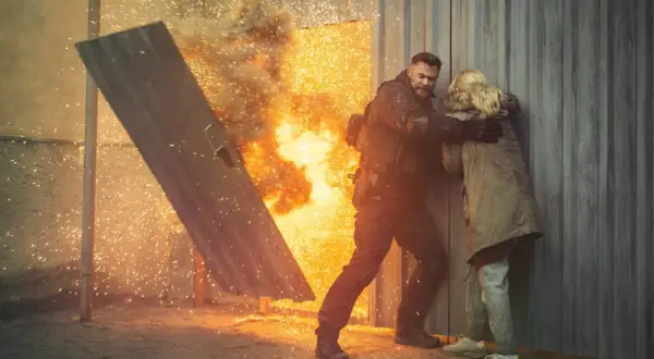Mężczyzna w kamizelce taktycznej chroni kobietę przed eksplozją, jak w najlepszych filmach akcji.