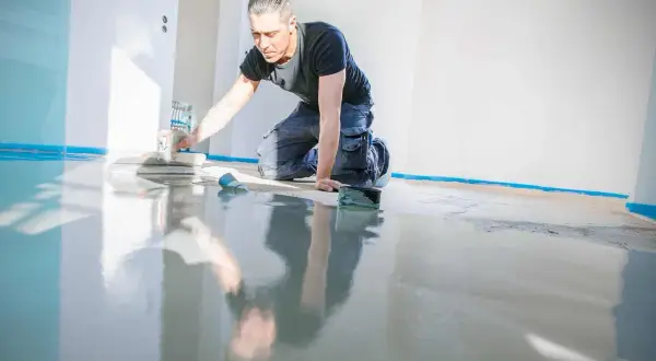 Mann kniet und beschichtet den Kellerboden mit einer Glättkelle. Der neue Boden glänzt spiegelnd.