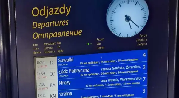 Tablica odjazdów pociągów z informacją o opóźnieniach, wskazująca na utrudnienia w ruchu pociągów. Zegar pokazuje aktualny czas.