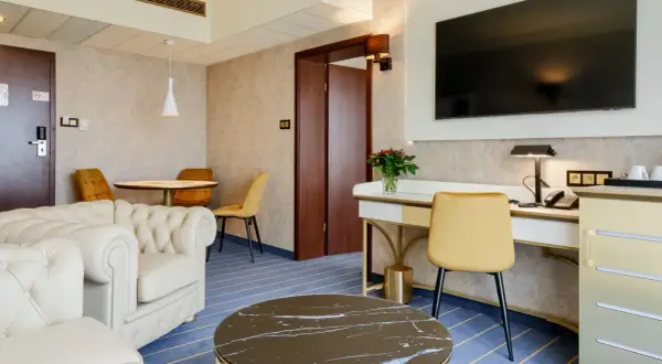Elegancki pokój w hotelu Diament Wrocław: wygodna sofa, biurko z telefonem i TV, stolik kawowy i okrągły stół z krzesłami.