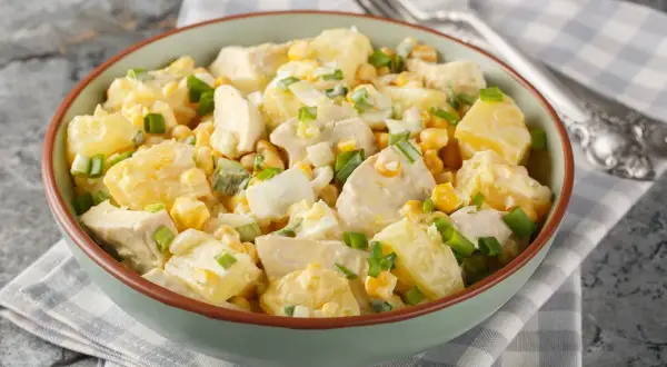 Insalata di pollo e patate cremosa con mais, uova sode e cipollotto fresco, servita in una ciotola verde.