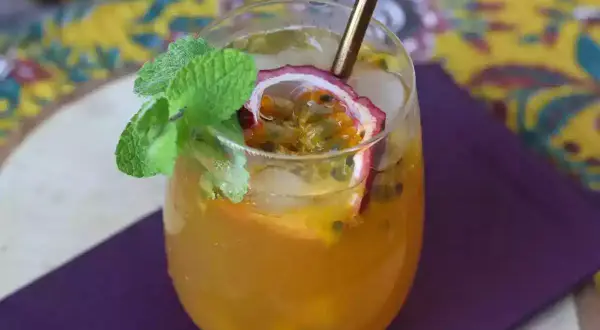 Un délicieux cocktail thé glacé aux fruits de la passion, garni de menthe fraîche et d'une tranche de fruit.
