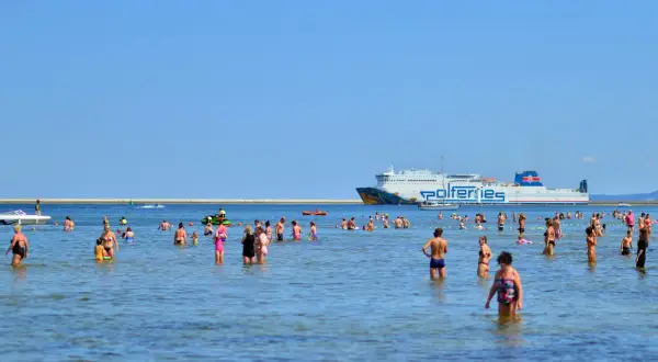 Ludzie kąpią się w morzu, a w tle płynie prom Polferries, który kursuje na trasie Świnoujście - Ystad.