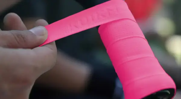 Mano applica nastro rosa su manubrio bici, mostrando la differenza tra grip e overgrip.