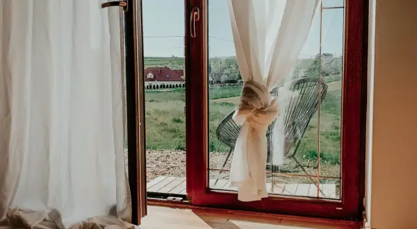Jak upiąć za długie firanki? Węzeł na zasłonie przy oknie z widokiem na wieś.