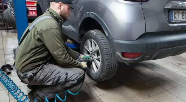 Mechanik w warsztacie dokonuje zmiany opon na zimowe, używając klucza pneumatycznego do odkręcenia śrub w kole samochodu.