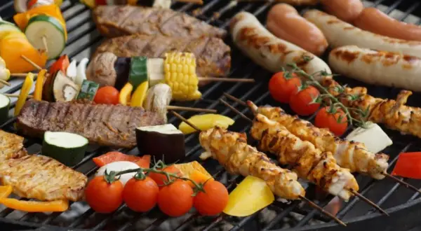 Na ruszcie grilluje się zdrowy grill: szaszłyki z kurczaka, wołowiny i warzyw, kiełbaski, pomidorki i kukurydza.