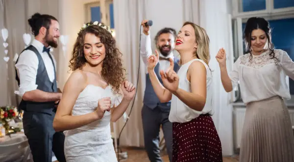 Brautpaar und Gäste tanzen ausgelassen. Frauen im lässigen Chic auf einer Hochzeit, die Braut trägt ein Spitzenkleid.