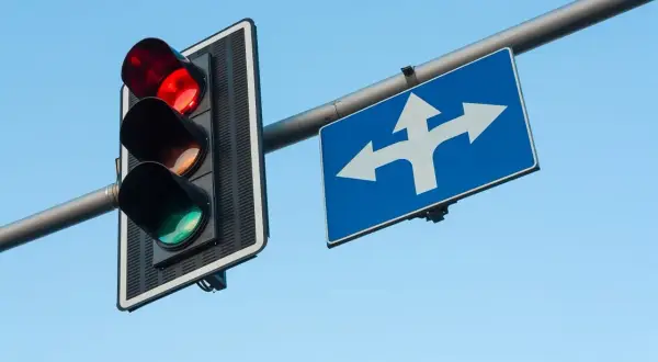 Czerwone światło na sygnalizatorze i znak wskazujący kierunki jazdy. Pamiętaj, co grozi za przejazd na czerwonym świetle – mandat i punkty karne.