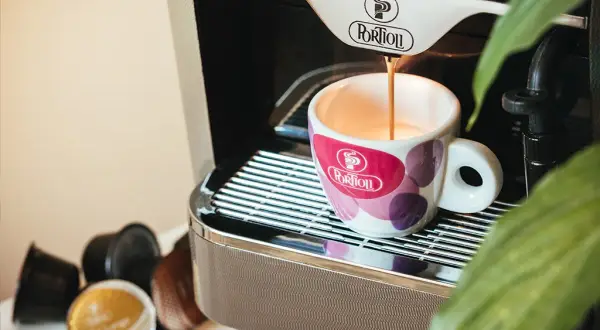 Espresso pouring into a patterned cup next to coffee capsules and a coffee machine.