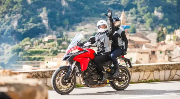 Para jadąca na czerwonym motocyklu Ducati, z pasażerem pozdrawiającym ręką.