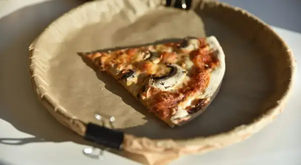Jeden kawałek pysznej pizzy z pieczarkami na brązowym papierze. Zastanawiasz się, ile kawałków ma pizza?