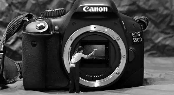 Miniaturowa postać czyści wnętrze aparatu Canon EOS 550D, pokazując, jak wyczyścić matrycę w aparacie.