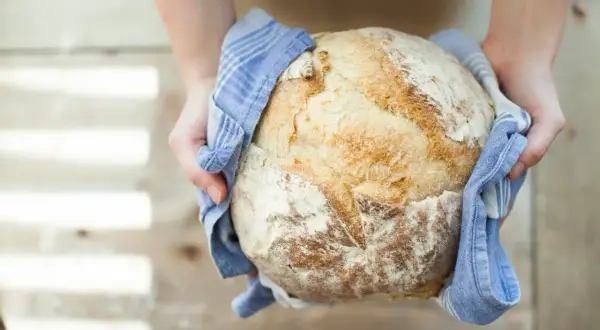 Mains d'une personne tenant un pain artisanal doré, tout juste sorti du four. Une belle réussite de recette pain.