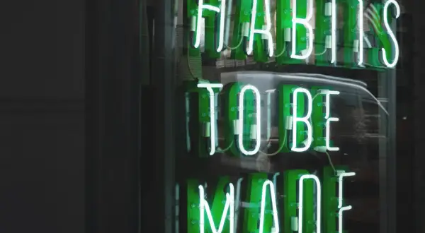 Zielone neony "HABITS TO BE MADE" przypominają o psychologii systemu nagród i kar, który kształtuje nasze nawyki.