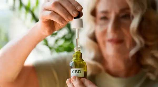 Kobieta trzyma buteleczkę olejku CBD. Zastanawia się, olejek CBD na co może jej pomóc w codziennym życiu.