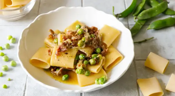 Piatto di paccheri conditi con piselli freschi e pezzetti croccanti di prosciutto crudo, un classico saporito.