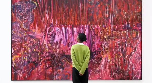 A person in a green sweater contemplates a vibrant, abstract painting, a visual guide on how to find up and coming artists.
