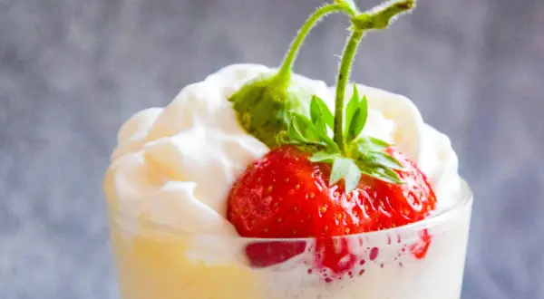 Deser zabaglione z truskawką i bitą śmietaną w szklance.