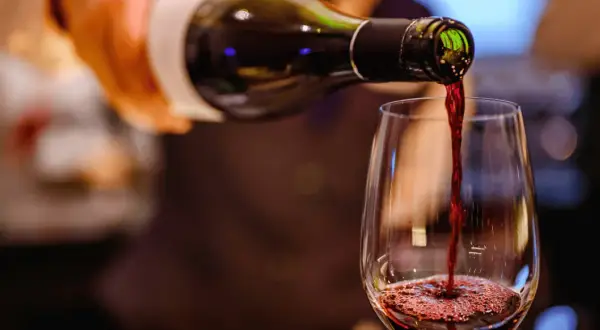 Czerwone wino leje się z butelki do kieliszka, tworząc piankę. Widać bogactwo **tannin w winie**, które nadają mu głębię.