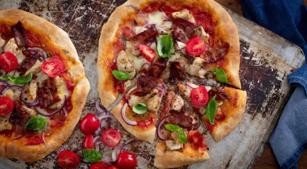 Två läckra pizzor med kyckling och bacon, toppade med körsbärstomater och basilika.