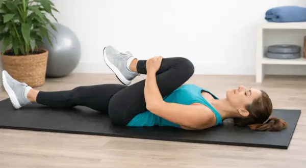 Une femme s'étire sur un tapis, genou plié vers la poitrine. C'est un exercice clé pour savoir comment j'ai guéri ma sciatique.