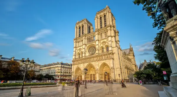 Vue de la cathédrale Notre-Dame de Paris sous un ciel bleu, avec des passants fantomatiques sur le parvis. Un avis sur ce monument emblématique.