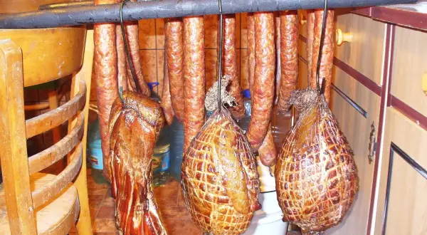 Wędzonki wiszą na drążku: kiełbasy, boczki i wędzonki w siatce. Idealne do marynaty do boczku.