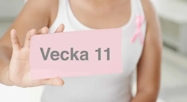 En person håller upp en rosa lapp med texten "Vecka 11". En rosa band-symbol syns på kläderna.