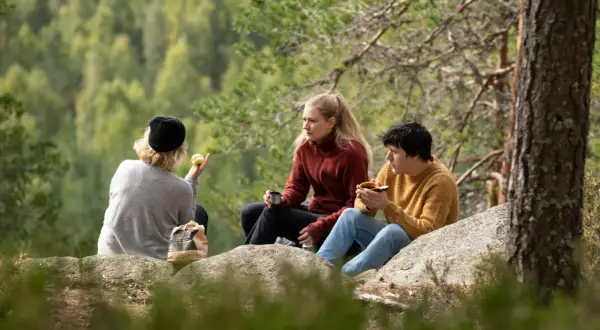 Vänner fikar på en klippa vid STF Undersvik med skogen som bakgrund.