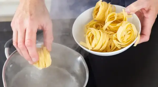 Ręce wkładają tagliatelle do wrzącej wody. Kluczowe jest, ile wody do makaronu, by był idealny.