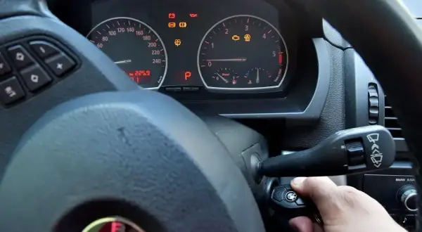 Ręka przekręca kluczyk w stacyjce BMW. Kontrolki na desce rozdzielczej świecą, ale rozrusznik nie kręci tylko cyka.