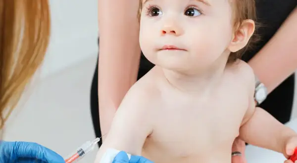 Małe dziecko otrzymuje szczepienie RSV. Ręka w niebieskiej rękawiczce trzyma strzykawkę, przygotowując się do podania zastrzyku.