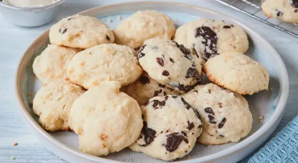 Leckere Cheesecake Cookies mit Schokoladenstückchen auf einem Teller, daneben eine Schüssel Frischkäse.