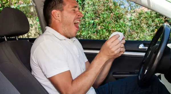 Hombre bostezando al volante, con un pañuelo en la mano. La fatiga puede afectar la conducción.
