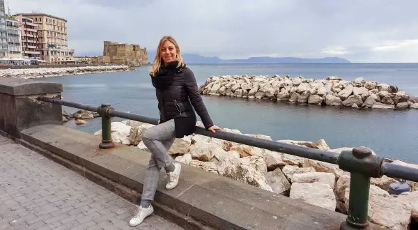 Donna sorridente sul lungomare di Napoli, con Castel dell'Ovo e il mare sullo sfondo. Un'ottima idea per cosa vedere a Napoli centro.