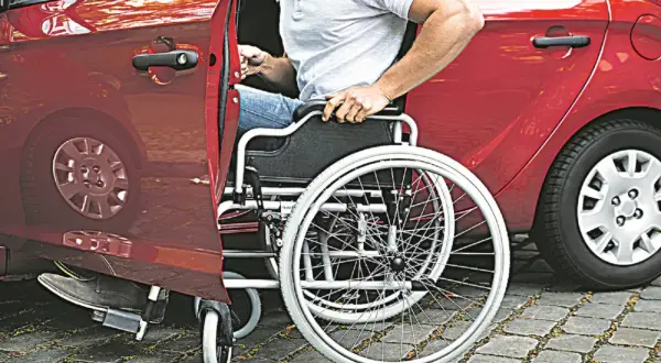 Un uomo in carrozzina si prepara a salire in un'auto rossa. Un caregiver ha aiutato nell'acquisto di un'auto adatta.