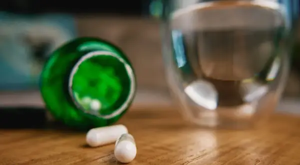 Kapsułki z berberyną obok szklanki wody. Czy berberyna a alkohol to dobre połączenie?