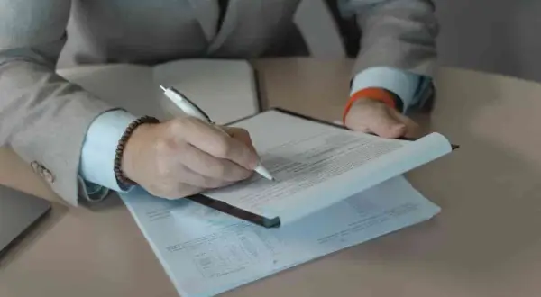 Rekruter w garniturze podpisuje dokumenty. Praca rekrutera to często analiza CV i rozmowy.