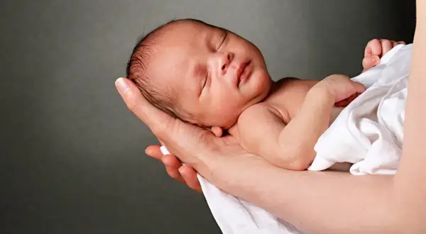 Słodki noworodek śpi w ramionach, otulony białym materiałem. To jak surogatka, która tuli swoje najcenniejsze skarby.