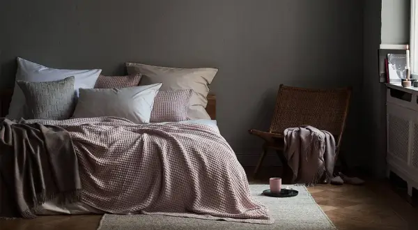 Gemütliches Schlafzimmer mit Bett in altrosa und grau, Korb-Sessel und Kerzenlicht.