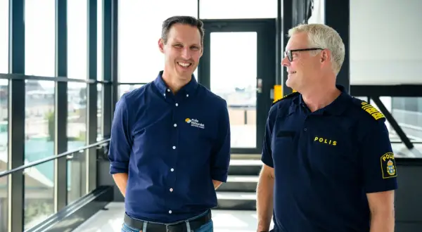 Två män ler mot varandra. Den ena bär en mörkblå skjorta med texten "Polis förbundet Bergslagen", den andra en polisuniform med texten "POLIS".
