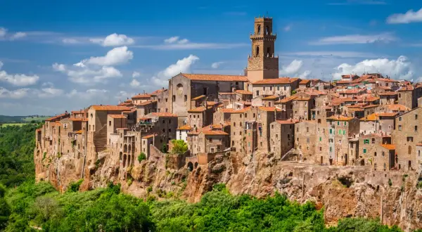 Vue panoramique de Magliano in Toscana, un village médiéval perché sur une falaise, avec ses maisons en pierre et son clocher imposant sous un ciel bleu.