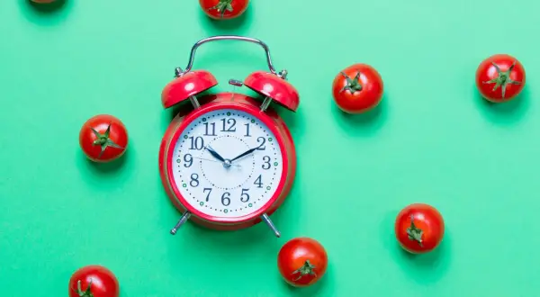Czerwony budzik i pomidorki na zielonym tle. Czy to symbol techniki "pomodoro" do efektywnej pracy?