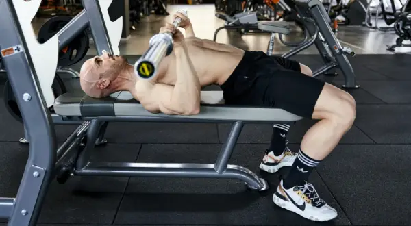 Uomo calvo si allena in palestra, sollevando un bilanciere su una panca. Un esempio di **super serie palestra** per un allenamento intenso.